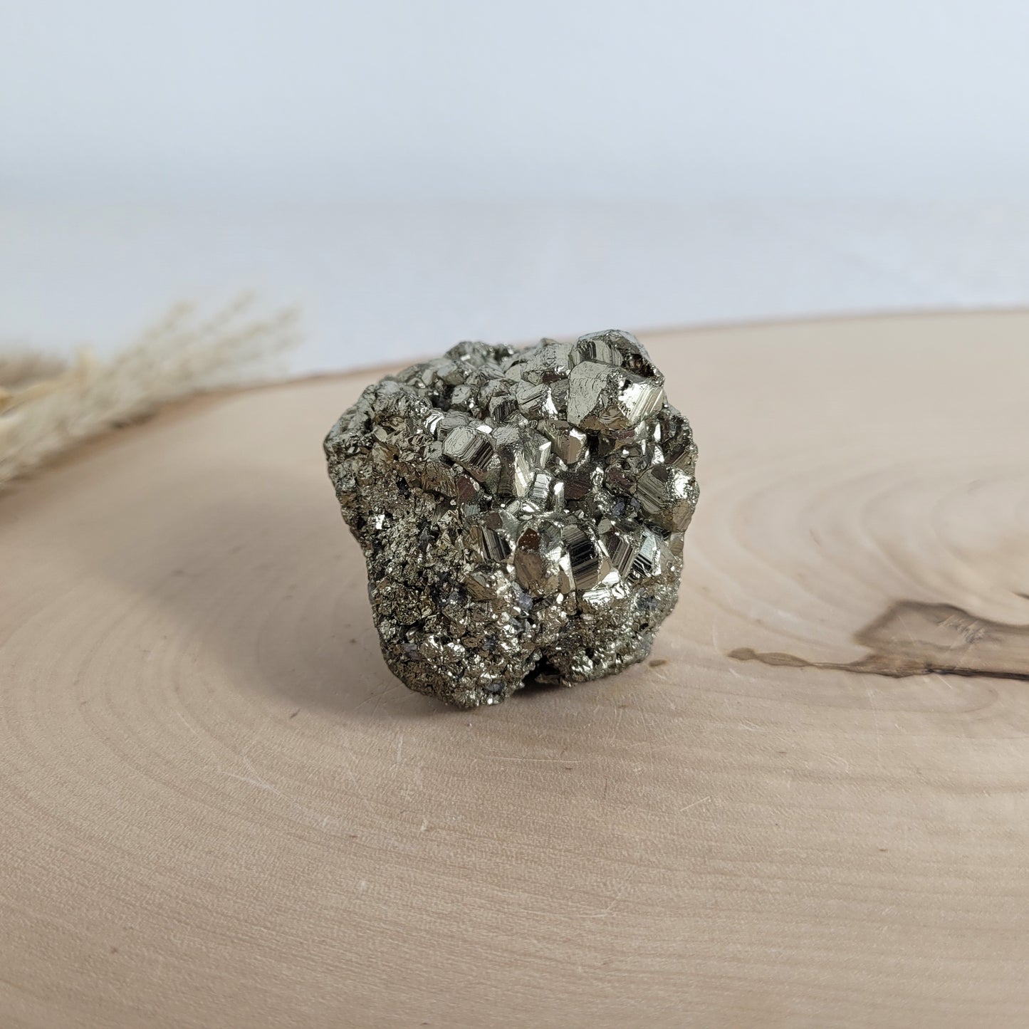 Pyrit-Kristallstufe auf einer Holzscheibe als natürlicher Hintergrund. Die metallisch glänzenden Kristalle heben sich kontrastreich vom warmen Holzton ab.