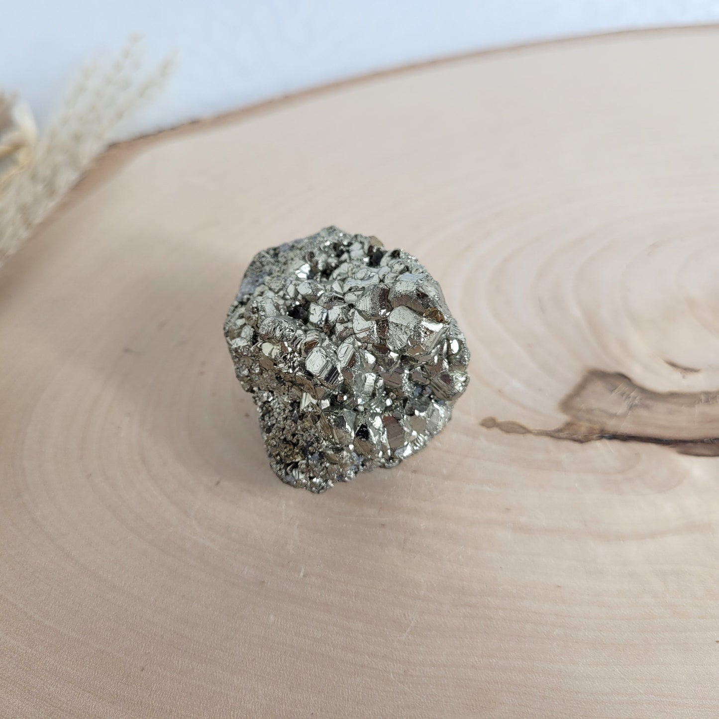 Pyrit-Kristallstufe auf einer Holzscheibe als natürlicher Hintergrund. Die metallisch glänzenden Kristalle heben sich kontrastreich vom warmen Holzton ab.
