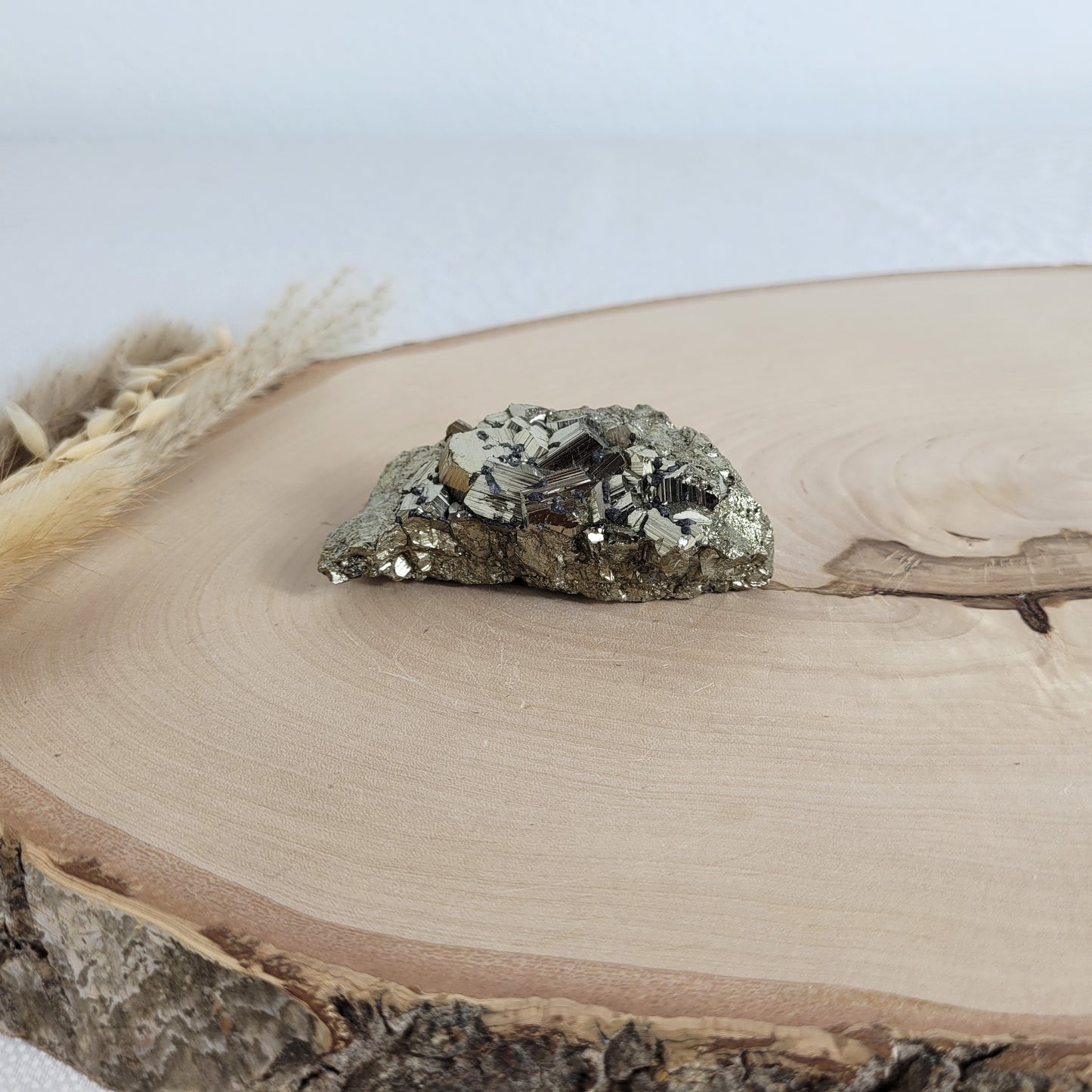 Pyrit-Kristallstufe auf einer Holzscheibe als natürlicher Hintergrund. Die metallisch glänzenden Kristalle heben sich kontrastreich vom warmen Holzton ab.