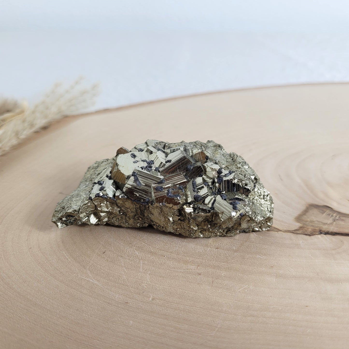 Pyrit-Kristallstufe auf einer Holzscheibe als natürlicher Hintergrund. Die metallisch glänzenden Kristalle heben sich kontrastreich vom warmen Holzton ab.