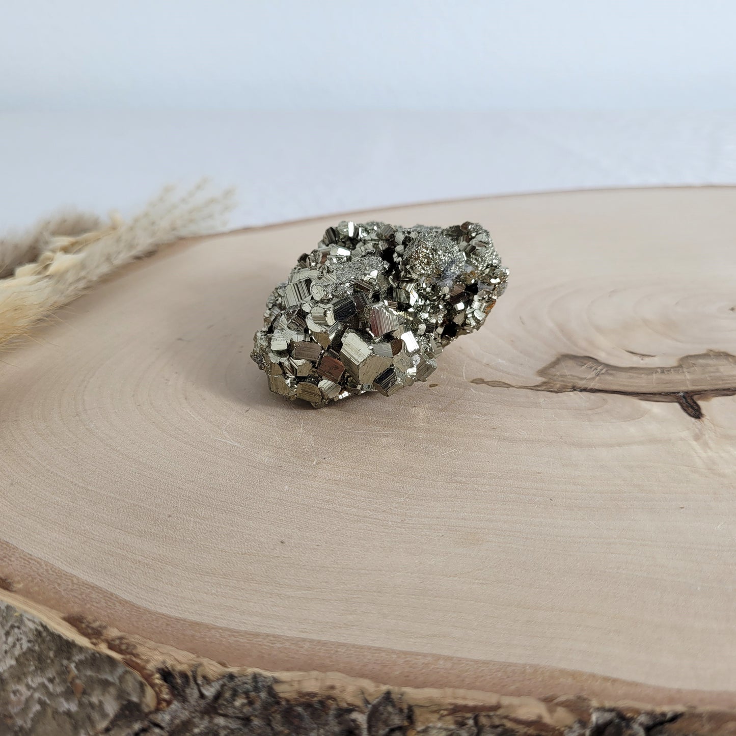Pyrit-Kristallstufe auf einer Holzscheibe als natürlicher Hintergrund. Die metallisch glänzenden Kristalle heben sich kontrastreich vom warmen Holzton ab.