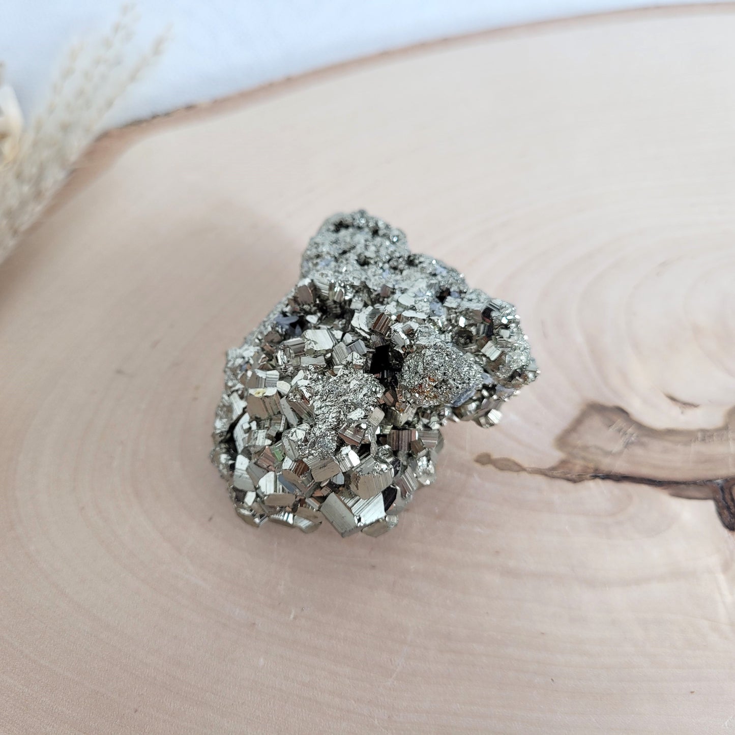 Pyrit-Kristallstufe auf einer Holzscheibe als natürlicher Hintergrund. Die metallisch glänzenden Kristalle heben sich kontrastreich vom warmen Holzton ab.