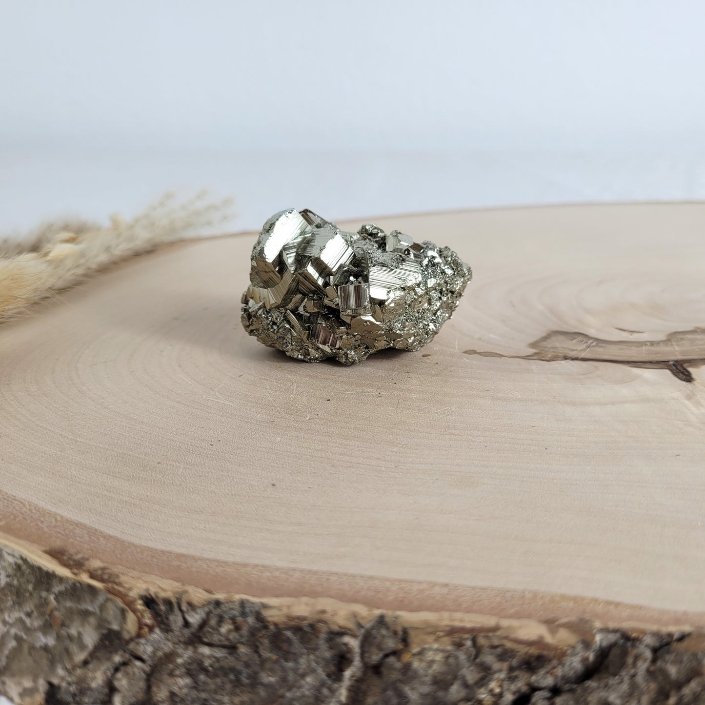 Pyrit-Kristallstufe auf einer Holzscheibe als natürlicher Hintergrund. Die metallisch glänzenden Kristalle heben sich kontrastreich vom warmen Holzton ab.