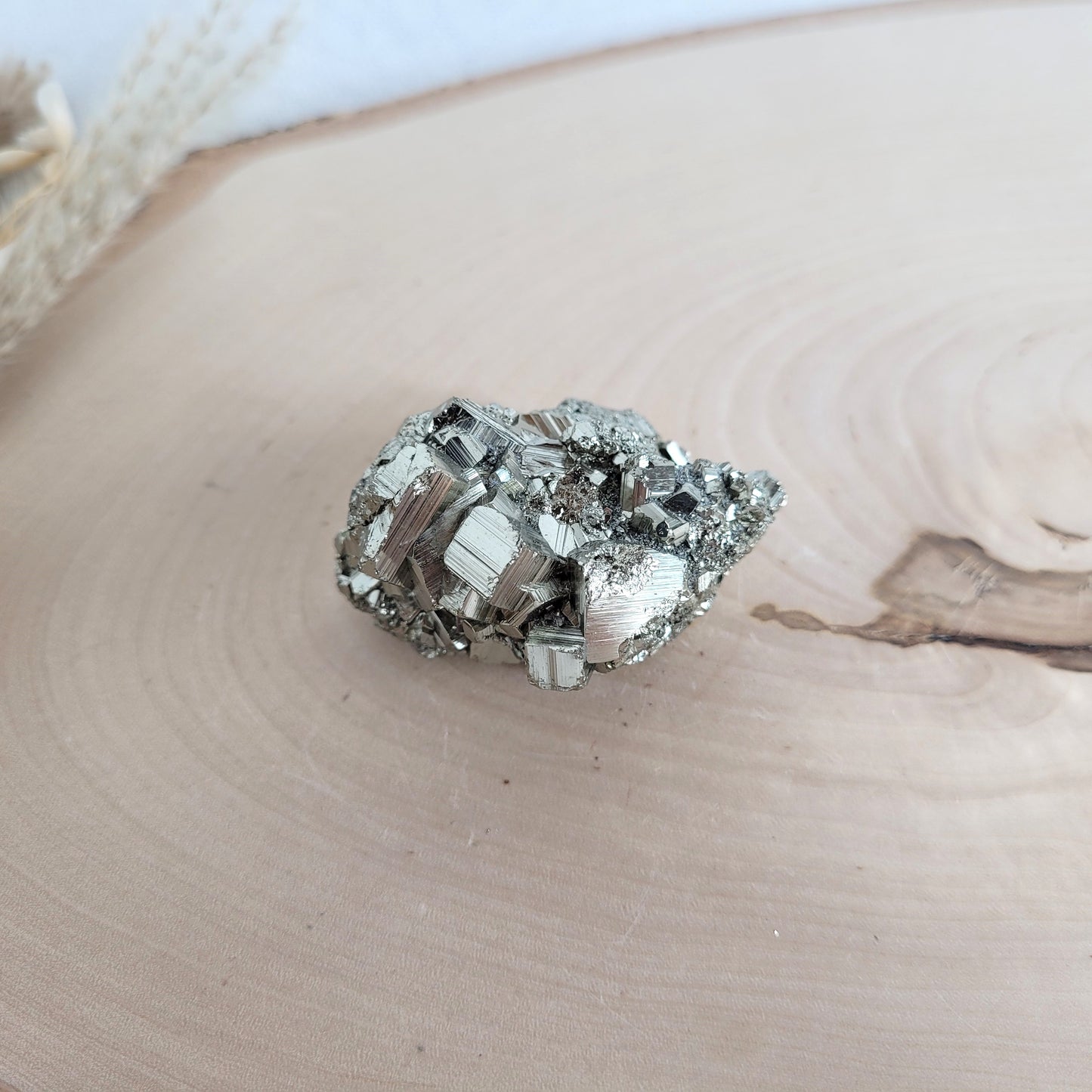 Pyrit-Kristallstufe auf einer Holzscheibe als natürlicher Hintergrund. Die metallisch glänzenden Kristalle heben sich kontrastreich vom warmen Holzton ab.