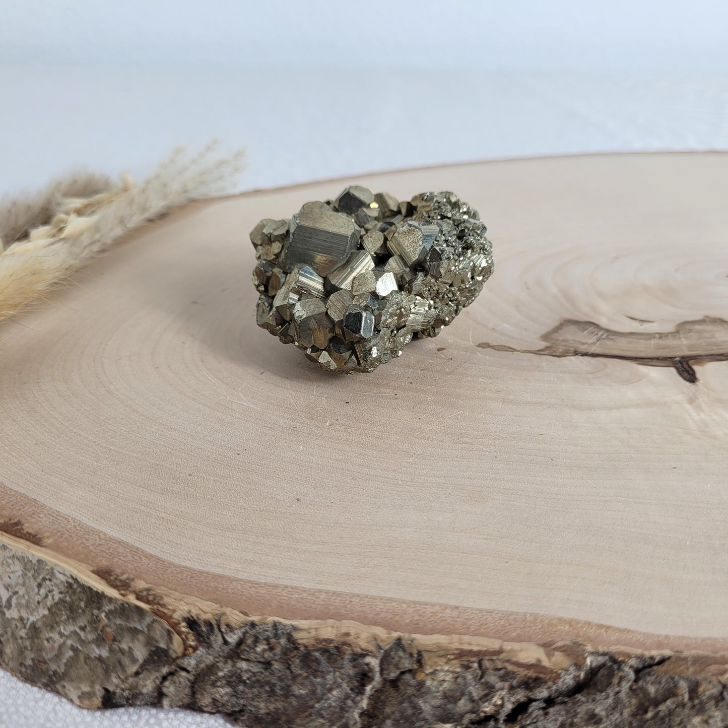 Pyrit-Kristallstufe auf einer Holzscheibe als natürlicher Hintergrund. Die metallisch glänzenden Kristalle heben sich kontrastreich vom warmen Holzton ab.