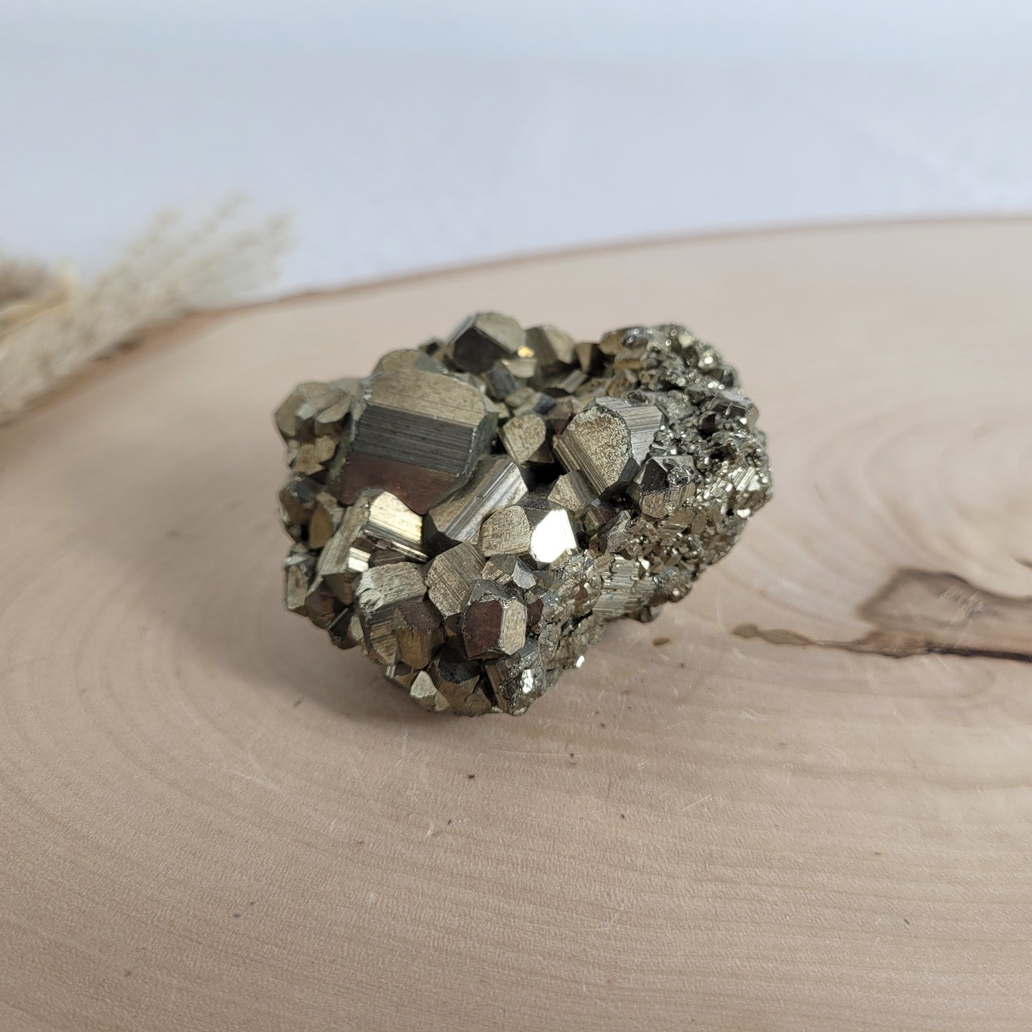 Pyrit-Kristallstufe auf einer Holzscheibe als natürlicher Hintergrund. Die metallisch glänzenden Kristalle heben sich kontrastreich vom warmen Holzton ab.