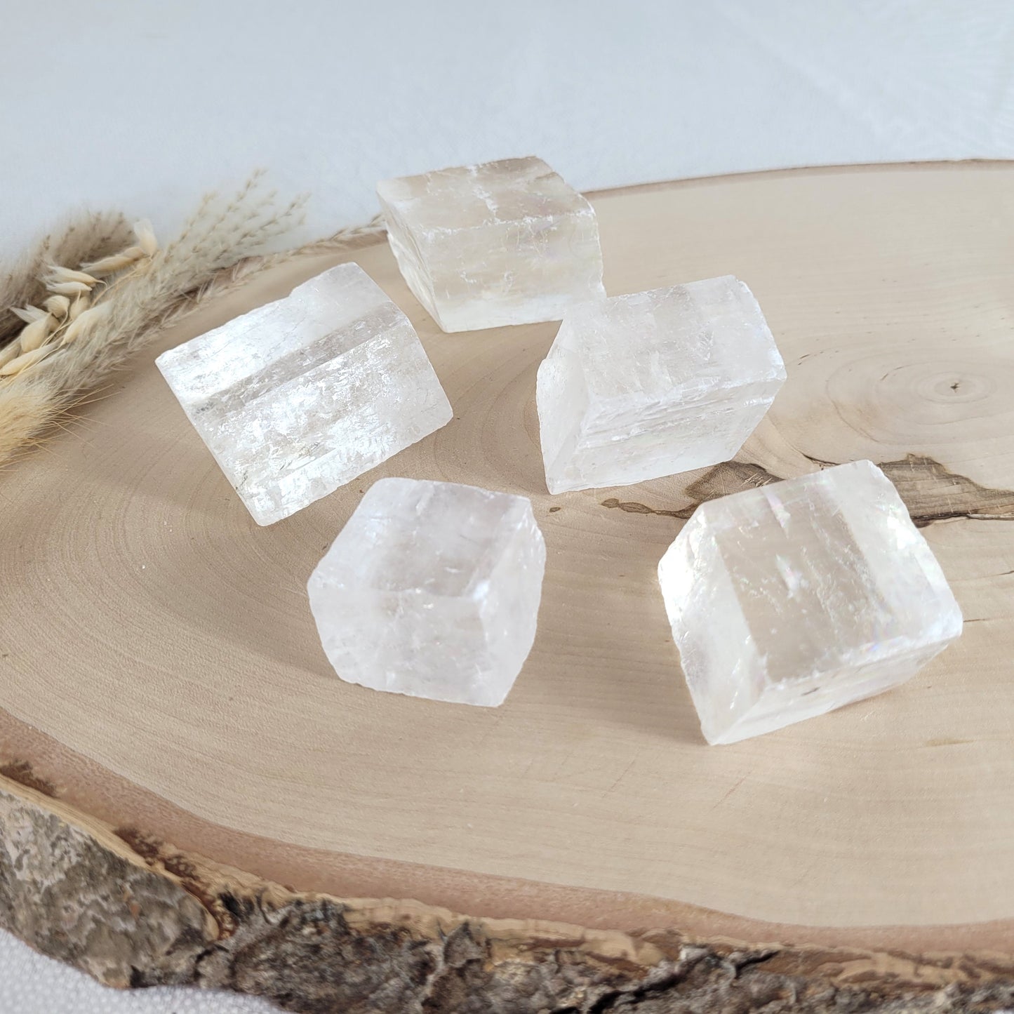 Doppelspat Kristall auf einer runden Holzscheibe präsentiert, naturbelassen mit sichtbarer Maserung – der Kristall zeigt bei Lichteinfall seine typische Doppelbrechung.