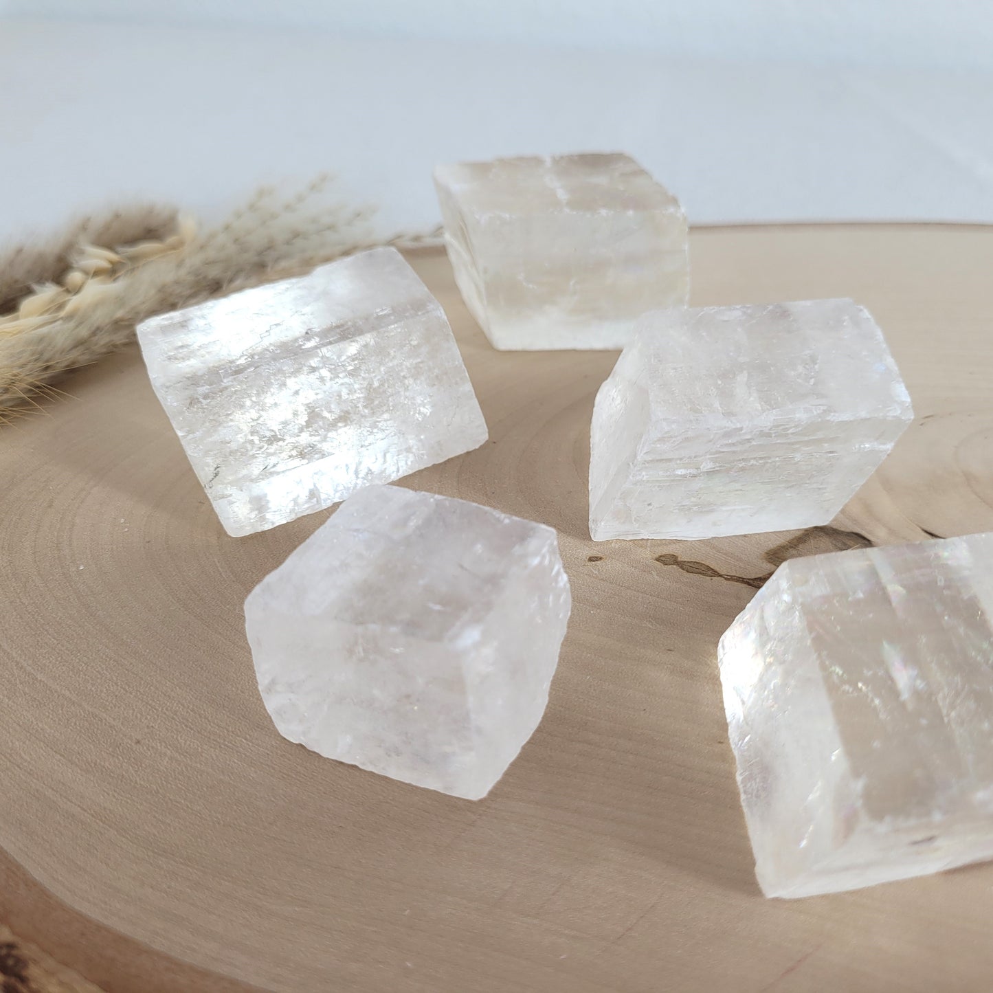 Doppelspat Kristall auf einer runden Holzscheibe präsentiert, naturbelassen mit sichtbarer Maserung – der Kristall zeigt bei Lichteinfall seine typische Doppelbrechung.