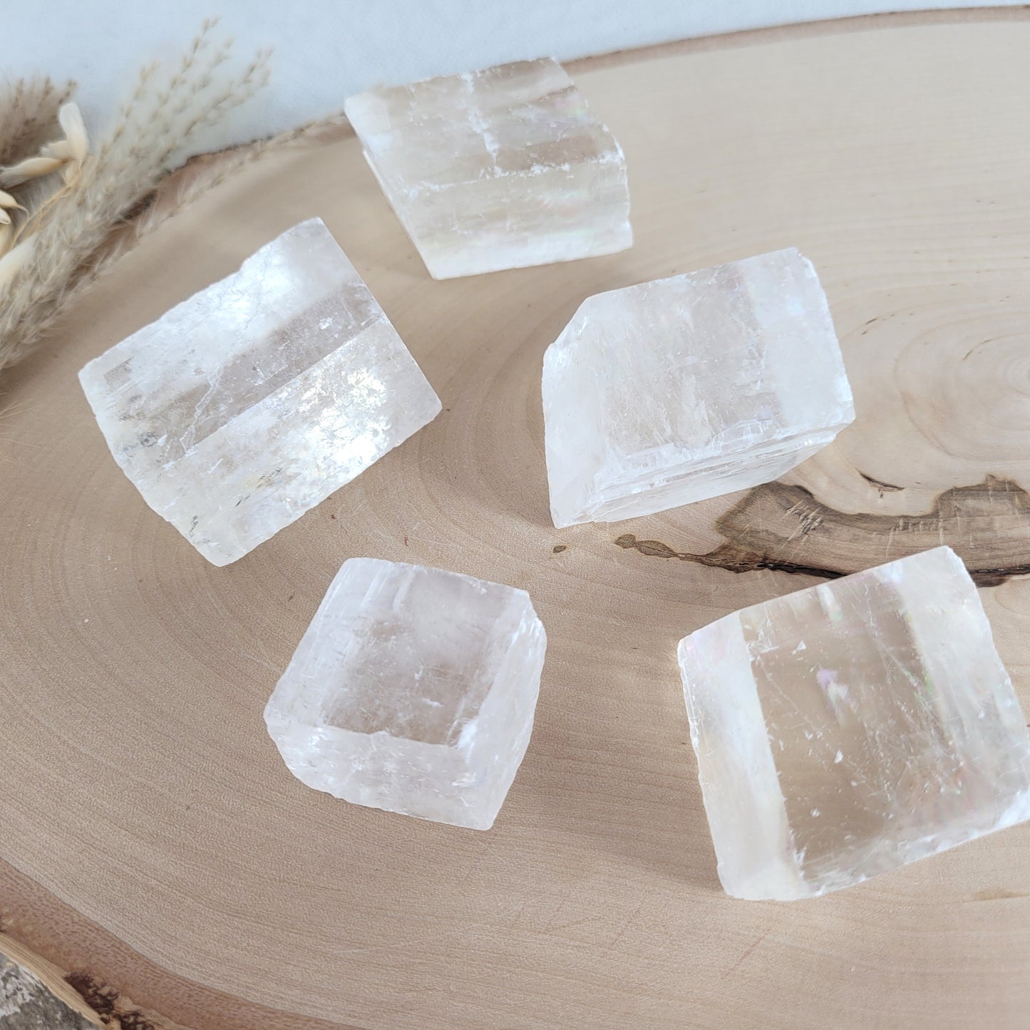 Doppelspat Kristall auf einer runden Holzscheibe präsentiert, naturbelassen mit sichtbarer Maserung – der Kristall zeigt bei Lichteinfall seine typische Doppelbrechung.