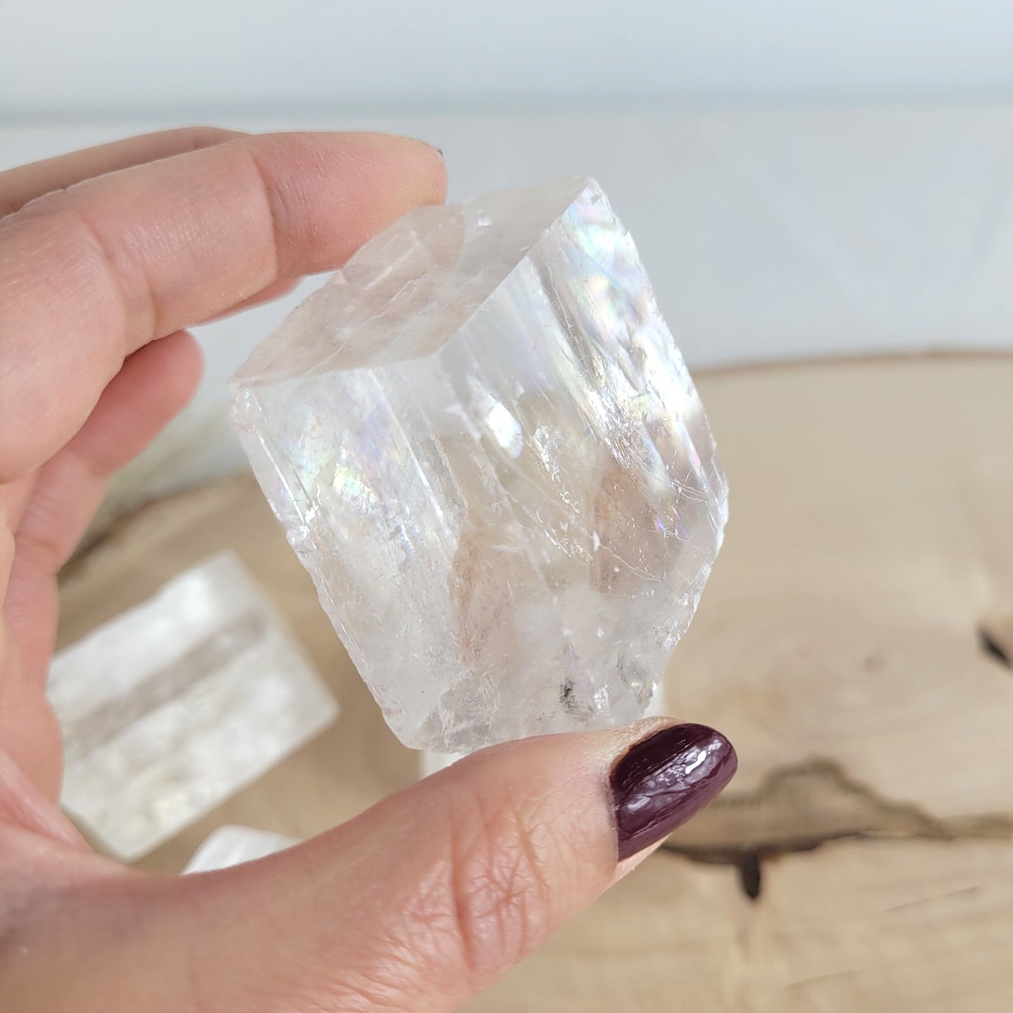 Doppelspat Kristall auf einer runden Holzscheibe präsentiert, naturbelassen mit sichtbarer Maserung – der Kristall zeigt bei Lichteinfall seine typische Doppelbrechung.