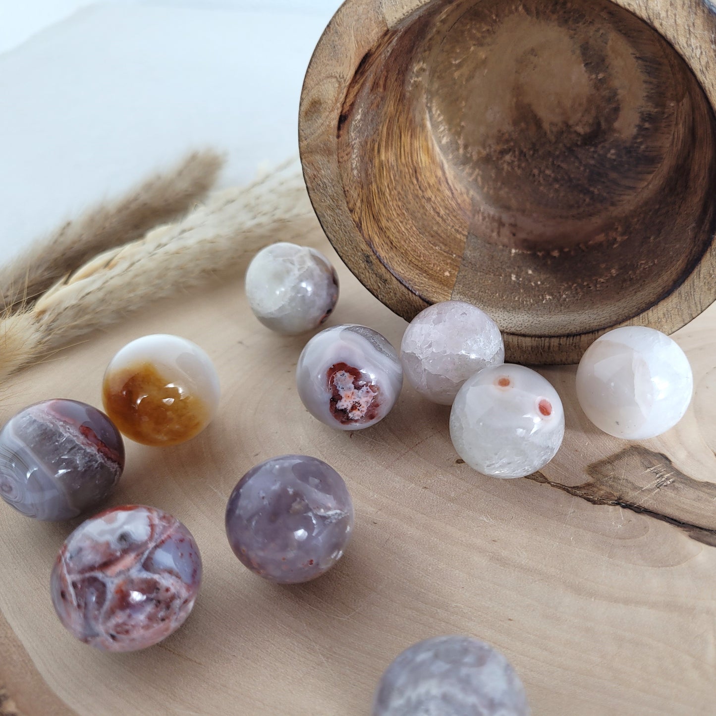 Chalcedon Kugel Mini geschliffen, liegend auf einer runden Holzscheibe mit sichtbarer Maserung – zeigt natürliche Farben, Muster und Kristallstrukturen.