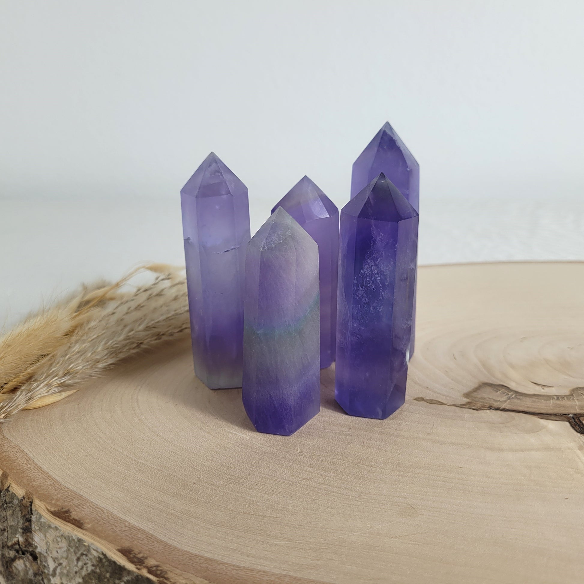 Set aus 5 geschliffenen Fluorit Spitzen in verschiedenen Größen, mit lila, grünen und weißen Farbverläufen, fotografiert auf einer Holzscheibe als Hintergrund.
