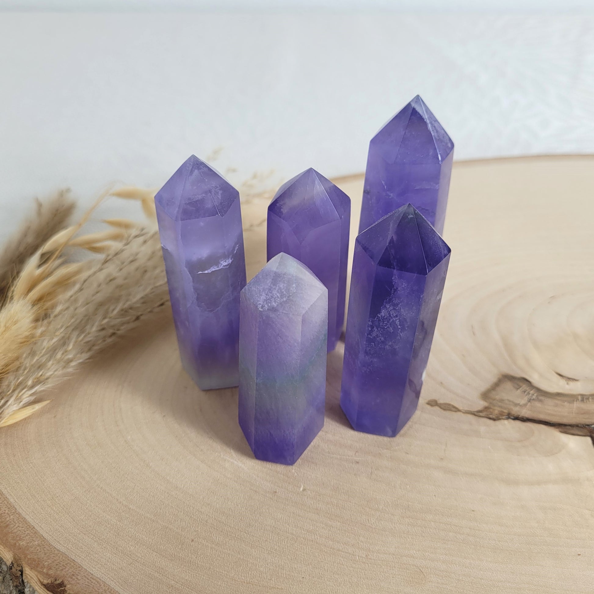 Set aus 5 geschliffenen Fluorit Spitzen in verschiedenen Größen, mit lila, grünen und weißen Farbverläufen, fotografiert auf einer Holzscheibe als Hintergrund.