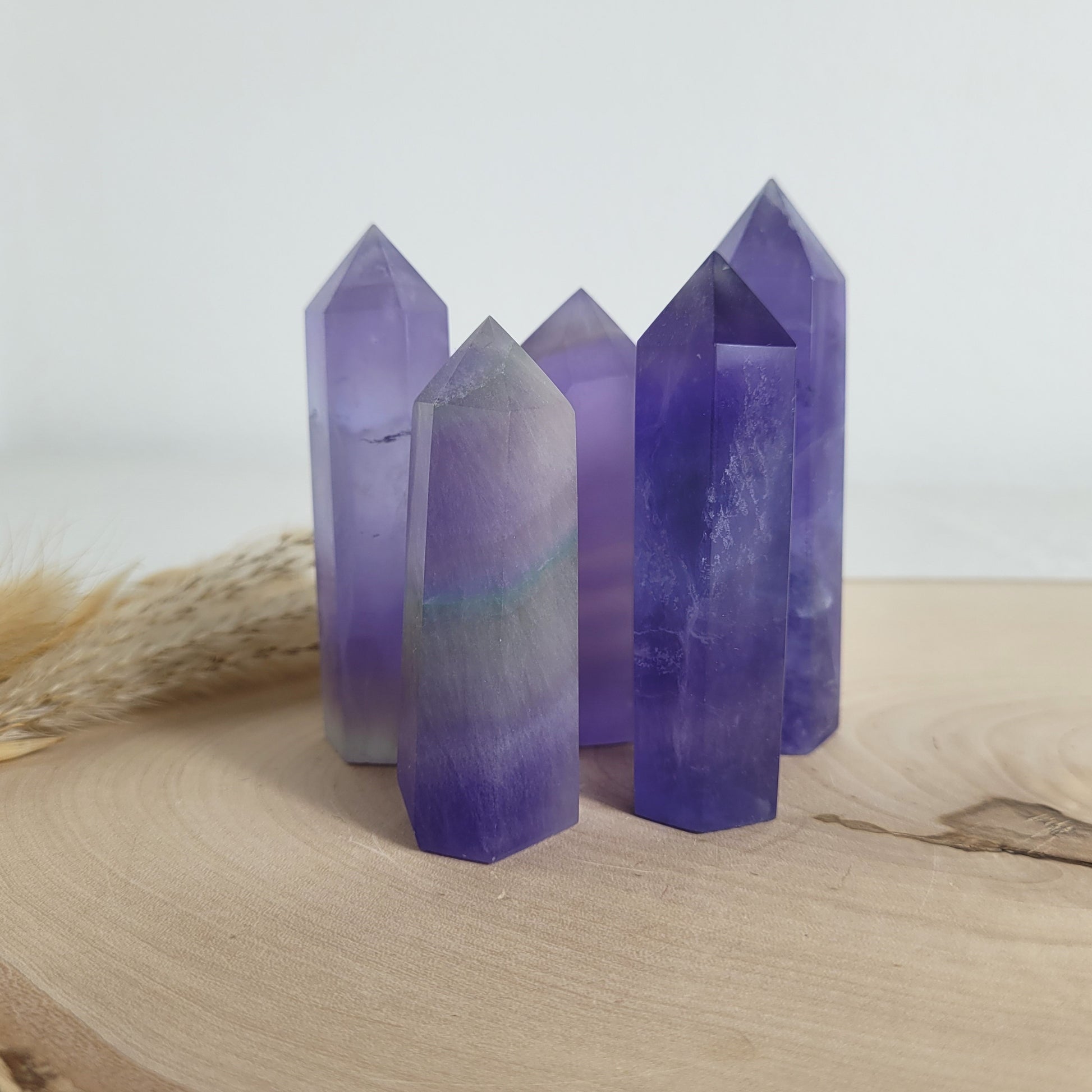 Set aus 5 geschliffenen Fluorit Spitzen in verschiedenen Größen, mit lila, grünen und weißen Farbverläufen, fotografiert auf einer Holzscheibe als Hintergrund.