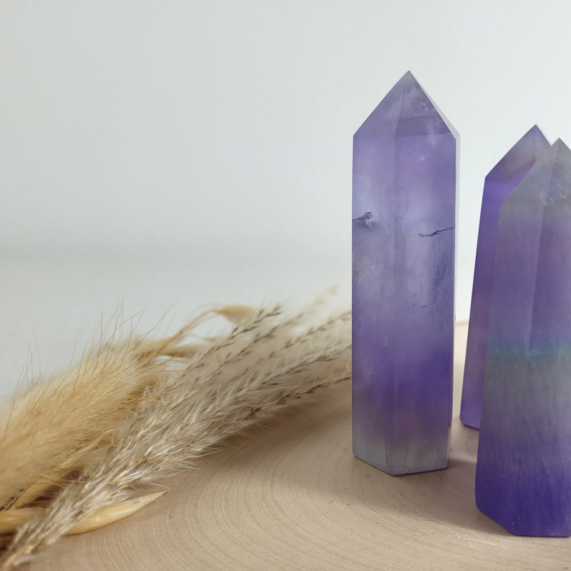 Set aus 5 geschliffenen Fluorit Spitzen in verschiedenen Größen, mit lila, grünen und weißen Farbverläufen, fotografiert auf einer Holzscheibe als Hintergrund.