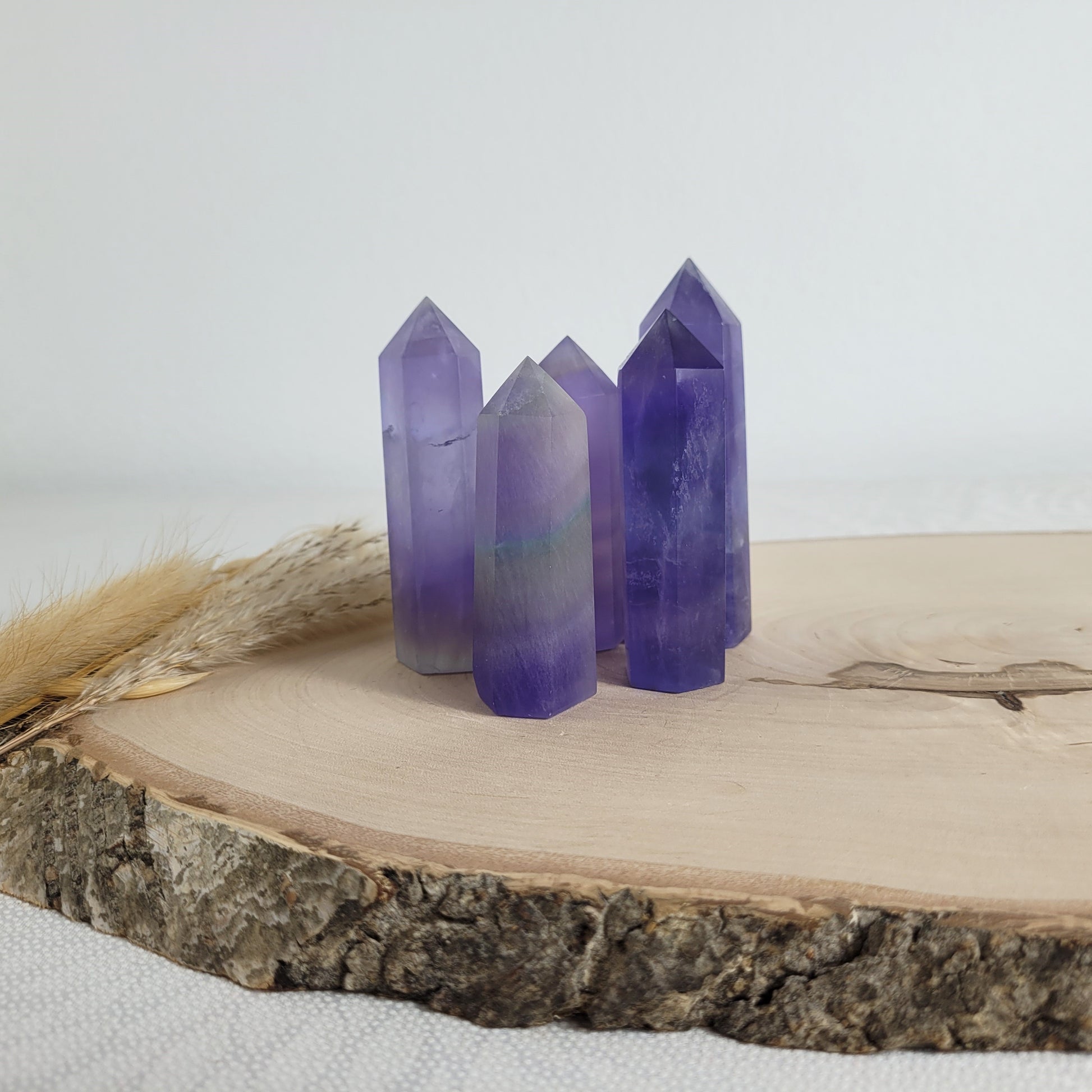 Set aus 5 geschliffenen Fluorit Spitzen in verschiedenen Größen, mit lila, grünen und weißen Farbverläufen, fotografiert auf einer Holzscheibe als Hintergrund.