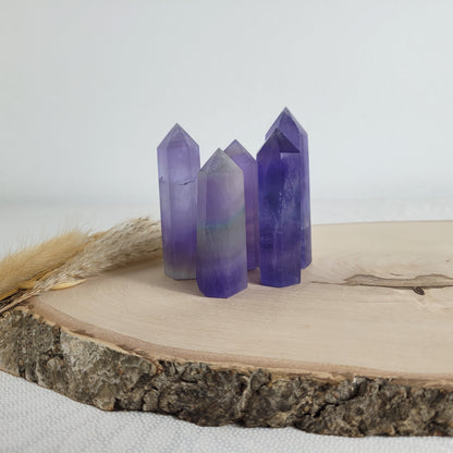 Set aus 5 geschliffenen Fluorit Spitzen in verschiedenen Größen, mit lila, grünen und weißen Farbverläufen, fotografiert auf einer Holzscheibe als Hintergrund.