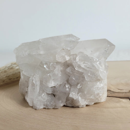 Bergkristall Naturstufe mit klaren Kristallen, platziert auf einer Holzscheibe, neutraler Hintergrund.
