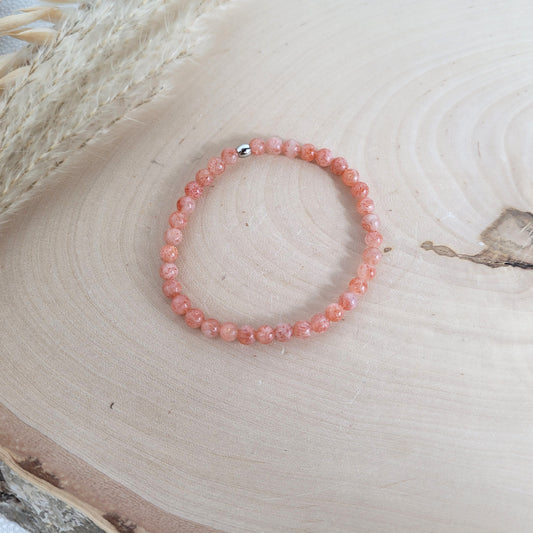 Elastisches Armband mit 4 mm Sonnenstein Perlen und Edelstahl Endperle, Holzscheibe als Hintergrund.