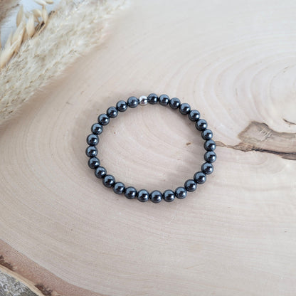 Elastisches Armband mit 6 mm Hämatit Perlen und Edelstahl Endperle, Holzscheibe als Hintergrund.