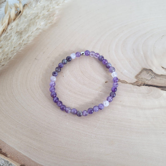 Elastisches Armband mit 5 mm Amethyst Perlen und Edelstahl Endperle, Holzscheibe als Hintergrund.