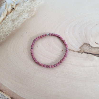 Elastisches Armband mit 4 mm Rhodonit Perlen und Edelstahl Endperle, Holzscheibe als Hintergrund.
