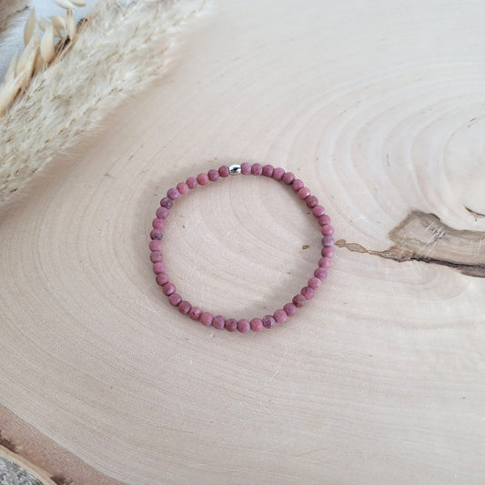 Elastisches Armband mit 4 mm Rhodonit Perlen und Edelstahl Endperle, Holzscheibe als Hintergrund.