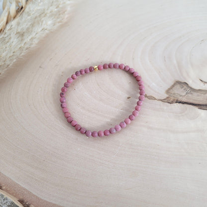 Elastisches Armband mit 4 mm Rhodonit Perlen und Silber 925 vergoldeter Endperle, Holzscheibe als Hintergrund.