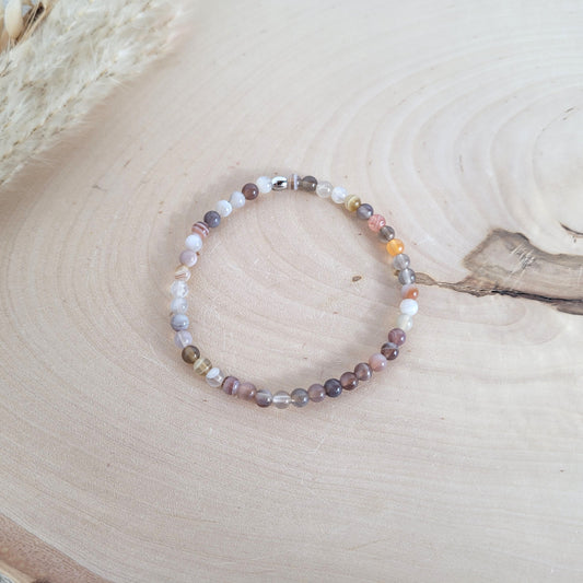 Elastisches Armband mit 4 mm Achat Perlen und Edelstahl Endperle, Holzscheibe als Hintergrund.
