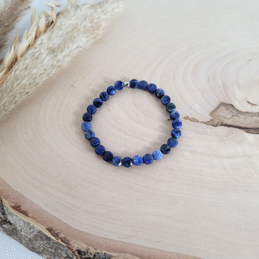 Elastisches Armband mit 6 mm Sodalith Perlen und Edelstahl Endperle, Holzscheibe als Hintergrund.