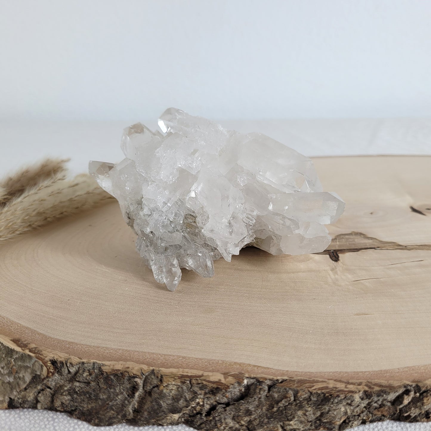 Bergkristall Naturstufe mit klaren Kristallen, platziert auf einer Holzscheibe, neutraler Hintergrund.