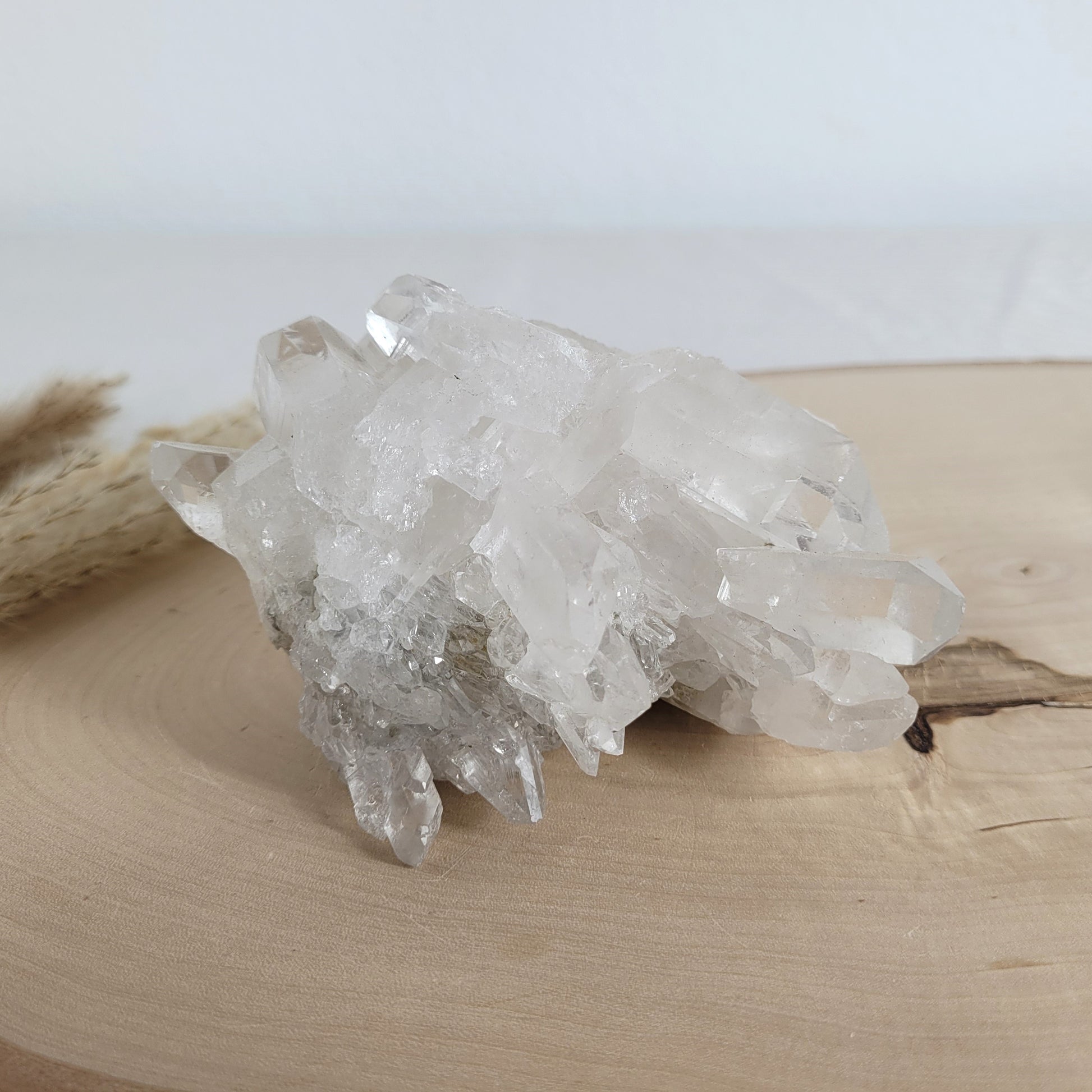 Bergkristall Naturstufe mit klaren Kristallen, platziert auf einer Holzscheibe, neutraler Hintergrund.