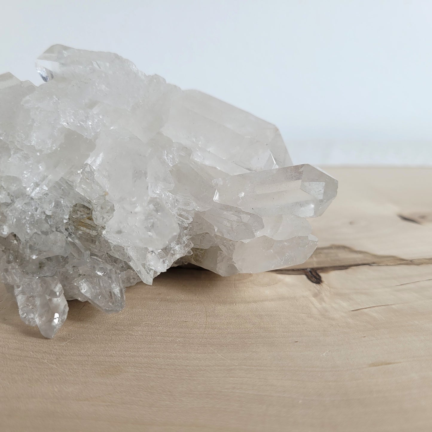 Bergkristall Naturstufe mit klaren Kristallen, platziert auf einer Holzscheibe, neutraler Hintergrund.