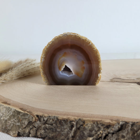 Achat Geode mit natürlicher Kristallöffnung und flacher Standfläche, platziert auf einer Holzscheibe.