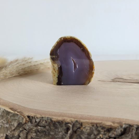 Achat Geode mit natürlicher Kristallöffnung und flacher Standfläche, platziert auf einer Holzscheibe.