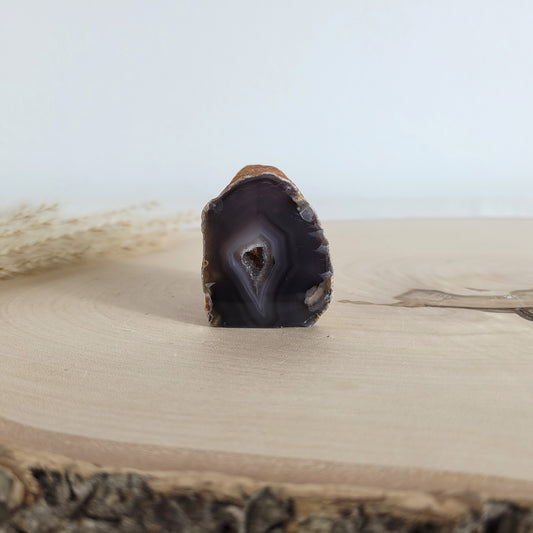 Achat Geode mit natürlicher Kristallöffnung und flacher Standfläche, platziert auf einer Holzscheibe.