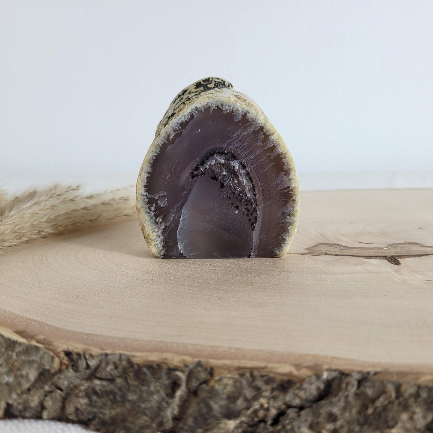 Achat Geode mit natürlicher Kristallöffnung und flacher Standfläche, platziert auf einer Holzscheibe.