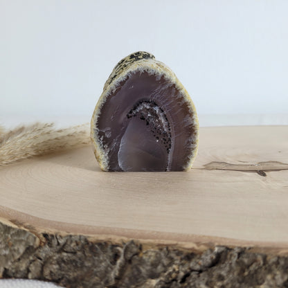 Achat Geode mit natürlicher Kristallöffnung und flacher Standfläche, platziert auf einer Holzscheibe.