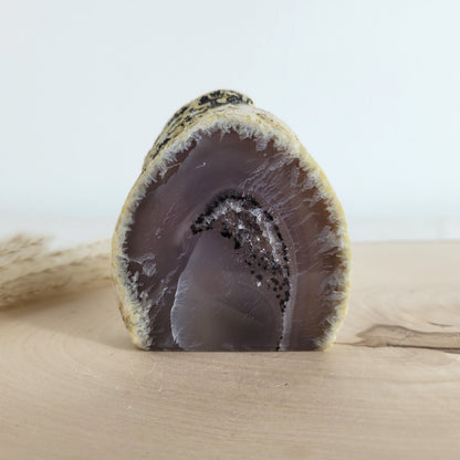 Achat Geode mit natürlicher Kristallöffnung und flacher Standfläche, platziert auf einer Holzscheibe.