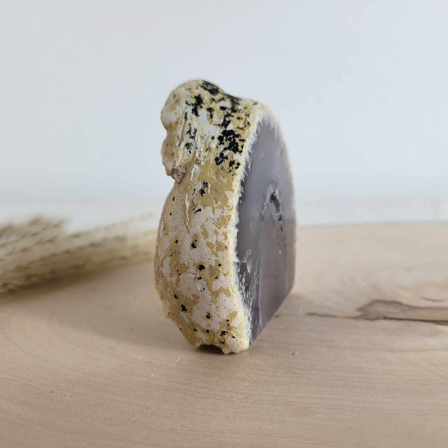 Achat Geode mit natürlicher Kristallöffnung und flacher Standfläche, platziert auf einer Holzscheibe.
