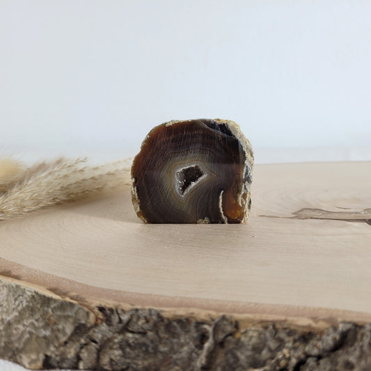 Achat Geode mit natürlicher Kristallöffnung und flacher Standfläche, platziert auf einer Holzscheibe.