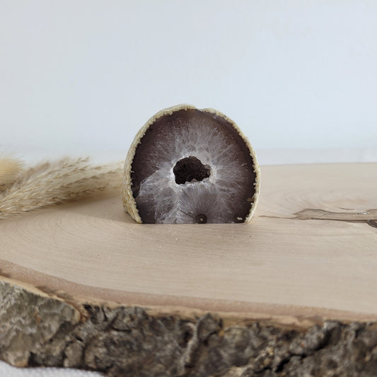 Achat Geode mit natürlicher Kristallöffnung und flacher Standfläche, platziert auf einer Holzscheibe.