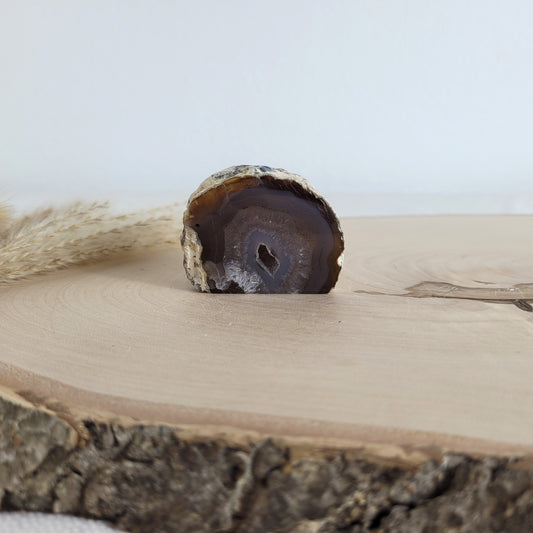 Achat Geode mit natürlicher Kristallöffnung und flacher Standfläche, platziert auf einer Holzscheibe.