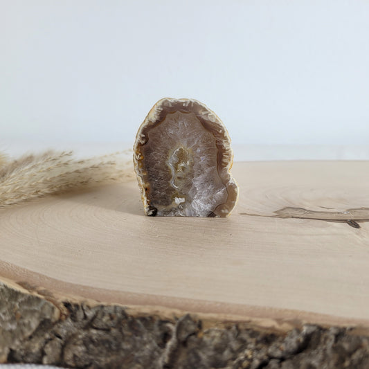 Achat Geode mit natürlicher Kristallöffnung und flacher Standfläche, platziert auf einer Holzscheibe.