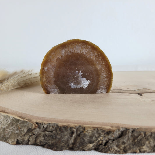 Achat Geode mit natürlicher Kristallöffnung und flacher Standfläche, platziert auf einer Holzscheibe.
