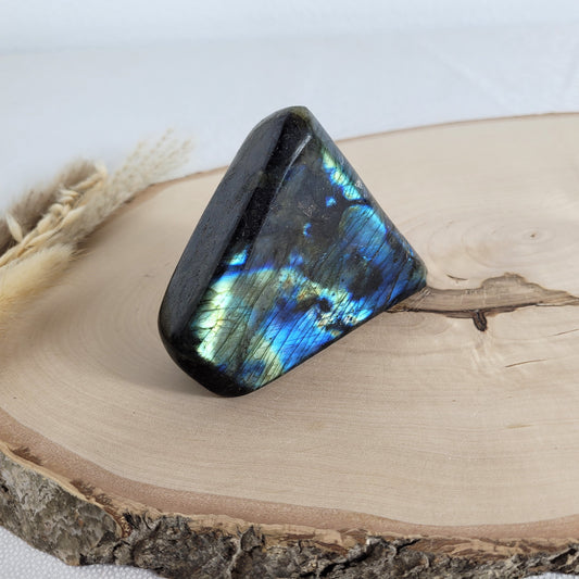 Labradorit Freiform mit natürlichem, intensivem Farbspiel, präsentiert auf einer Holzscheibe. Die typische Lamellenstruktur bricht das Licht auf besondere Weise und macht das Stück zu einem besonderen Blickfang.