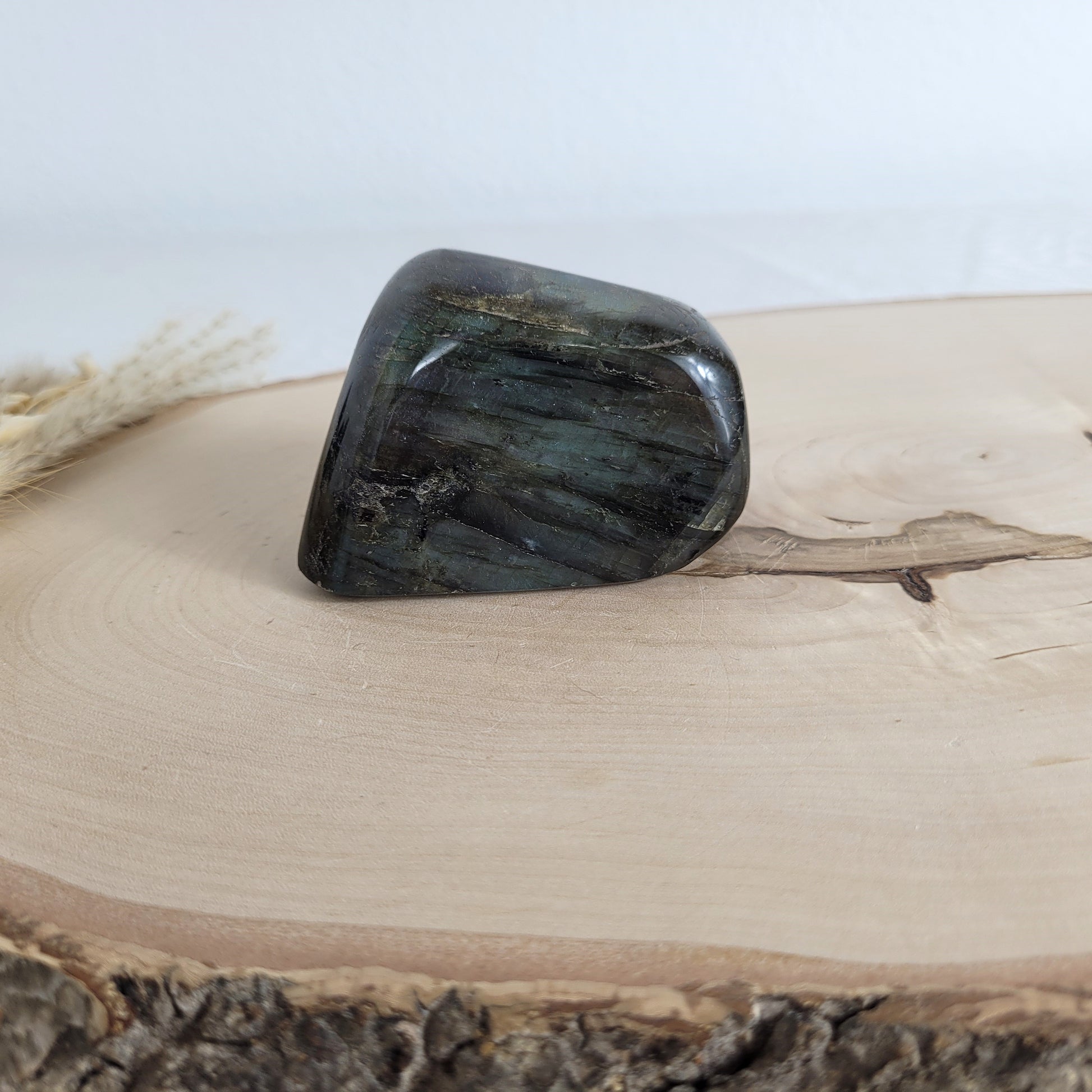 Labradorit Freiform mit natürlichem, intensivem Farbspiel, präsentiert auf einer Holzscheibe. Die typische Lamellenstruktur bricht das Licht auf besondere Weise und macht das Stück zu einem besonderen Blickfang.