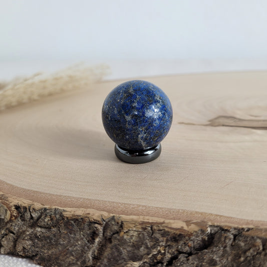 Lapis Lazuli Kugel mit intensiver blauer Farbe und goldglänzenden Pyrit-Einschlüssen, dekorativ platziert auf einer natürlichen Holzscheibe.