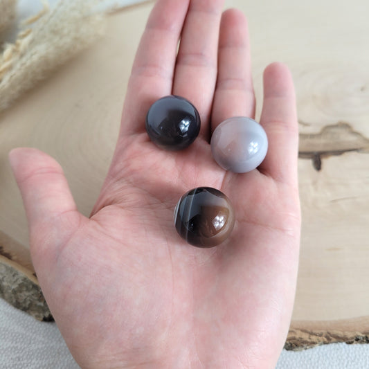 Botswana Achat Kugel Mini mit natürlichen Farben und feinen Bänderungen, präsentiert auf einer runden Holzscheibe zur Hervorhebung der einzigartigen Musterung.