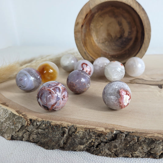 Chalcedon Kugel Mini geschliffen, liegend auf einer runden Holzscheibe mit sichtbarer Maserung – zeigt natürliche Farben, Muster und Kristallstrukturen.